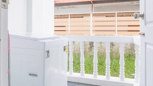 A balcony with a white railing, a white door, and a view of a building with a red roof. - Charming Studio Suite - Private Washer  (Chalong)