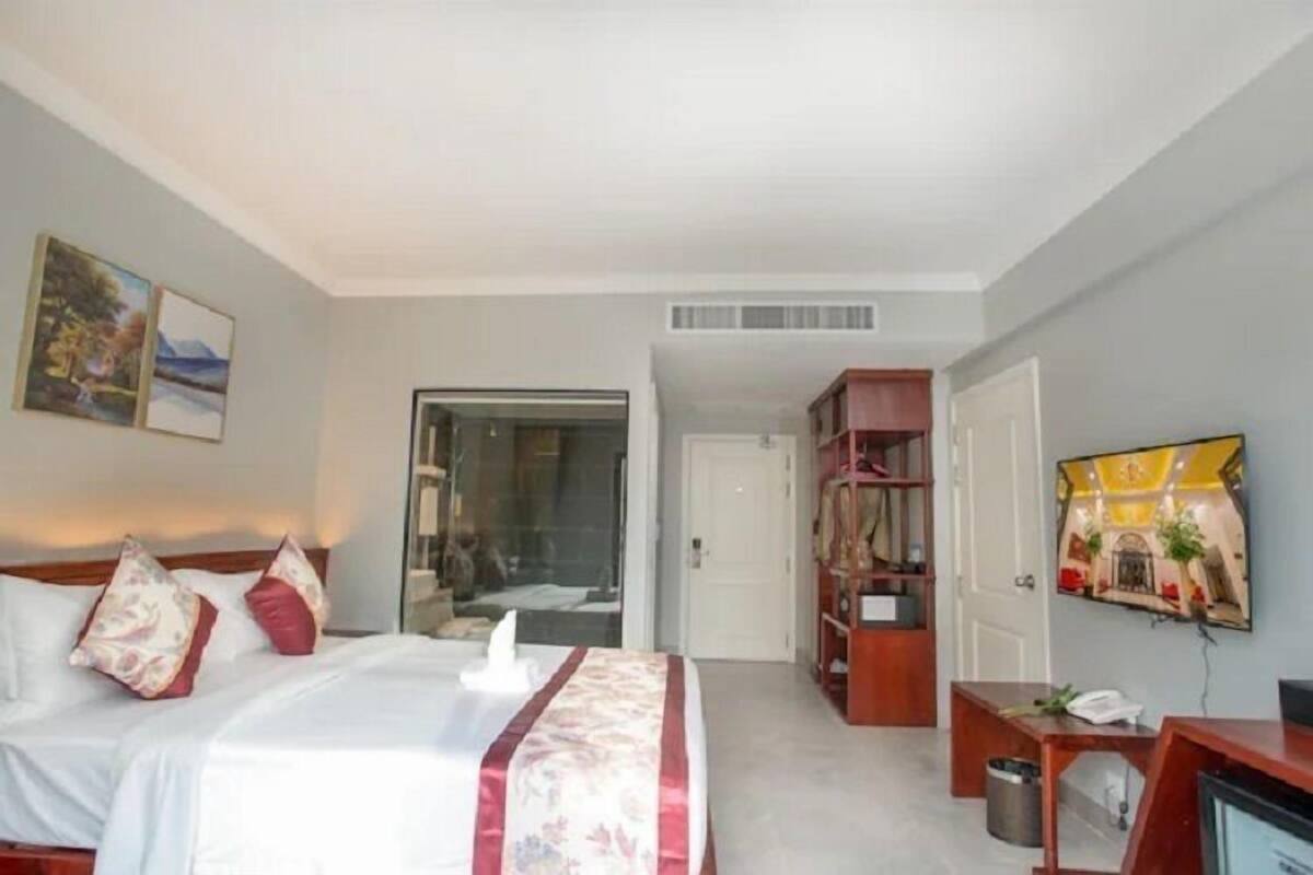 Quarto de hotel com cama, escrivaninha, televisão e estante de livros.