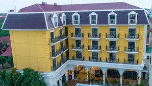 Um hotel com vários andares, fachada amarela, diversas varandas e uma área externa coberta com assentos.