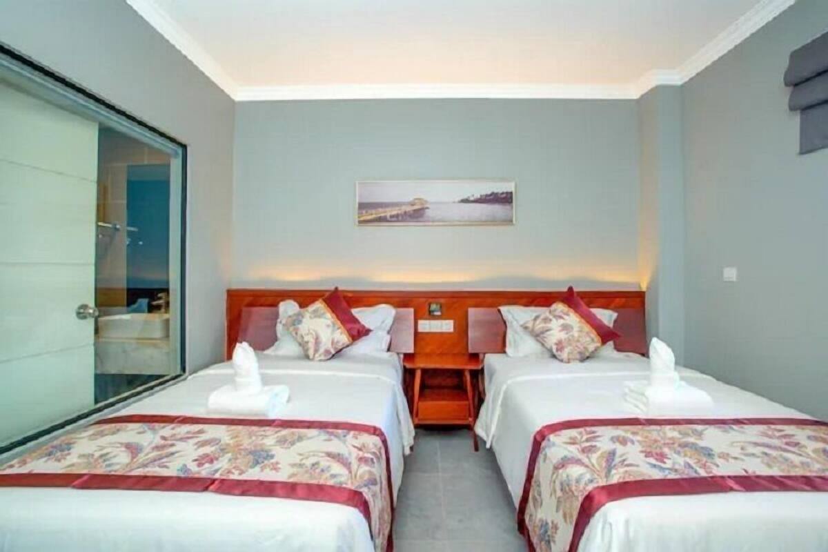 Quarto de hotel com duas camas, um quadro na parede e vista para o mar.