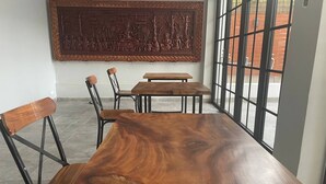 Uma longa mesa de madeira com cadeiras em um quarto com janelas amplas e um elemento decorativo na parede.