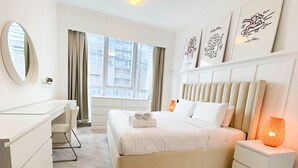 A hotel room with a bed, bedside tables, a desk, and a large window with curtains.