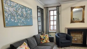 Un salon avec un canapé gris, un tableau abstrait bleu, une cheminée et un miroir.