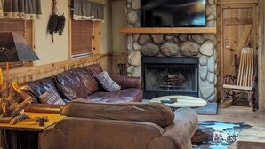 Een gezellig houten interieur met een stenen openhaard, lederen meubels en een bevestigde televisie.