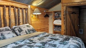 Een knus kamer in een blokhut met een bed, houten wanden, een lamp en een kledingkast.