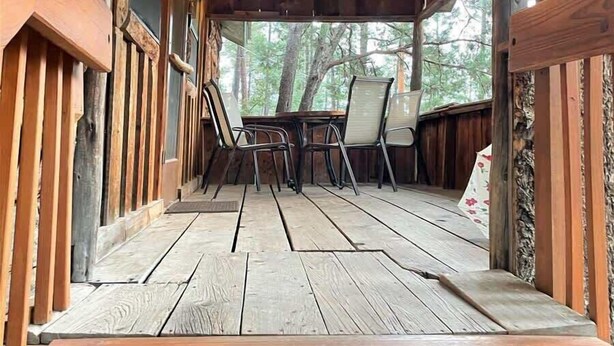 Een houten terras met een tafel en stoelen, omgeven door houten wanden en een schuin dak.