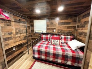 Un dormitorio acogedor con una colcha escocesa, una almohada roja y blanca y una ventana con persianas.