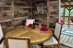 Una mesa redonda de madera con platos rojos y copas de vino, rodeada de sillas blancas acolchadas.