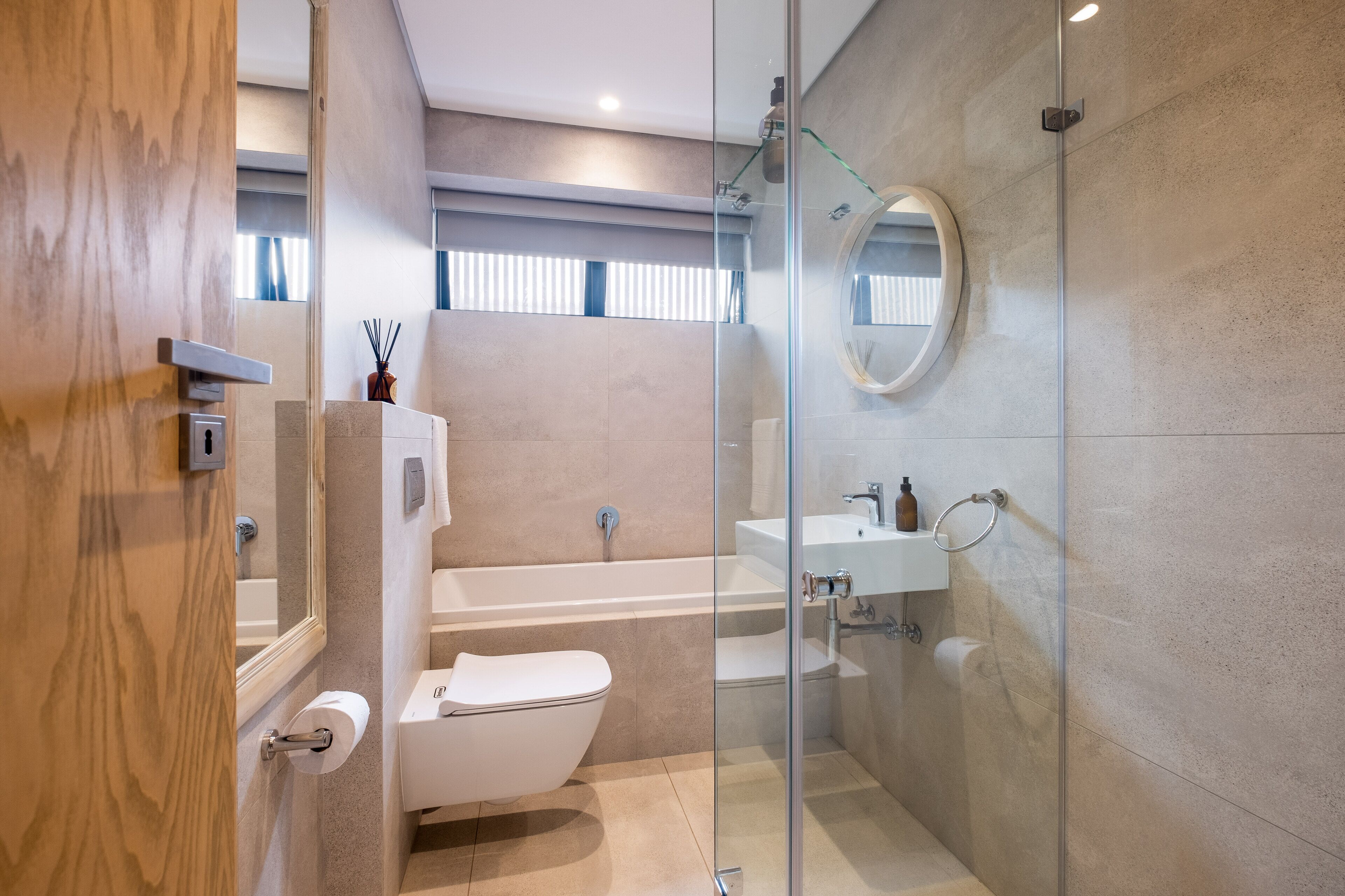 A modern bathroom with a glass shower enclosure, a white toilet, and a sink with a mirror.