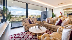 A modern living room with a large window, leather sofas, a white coffee table, and a red patterned rug. - 1 Savili - Zululami (Ballito)
