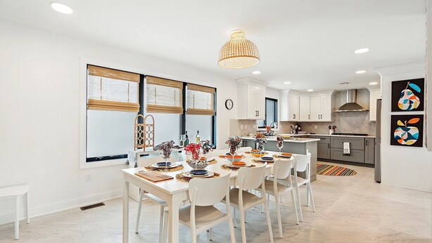A modern kitchen with white cabinetry, a central island, and a dining area with white chairs and a table set for a meal.