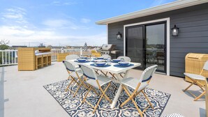 An outdoor patio with a dining table set for six, surrounded by wicker chairs, a grill, and a wicker basket.