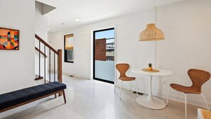 A modern interior with a bench, wicker chairs, a round table, and a hanging light fixture.