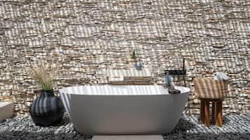Relax in a serene outdoor space with a bathtub surrounded by pebbles and a lush green plant.