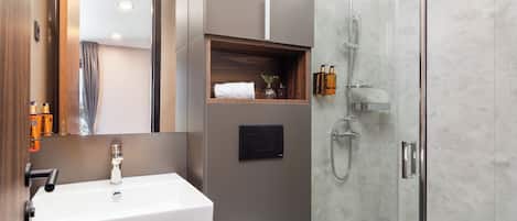 A modern bathroom with a large white sink, a glass shower enclosure, and a wooden shelf with toiletries.