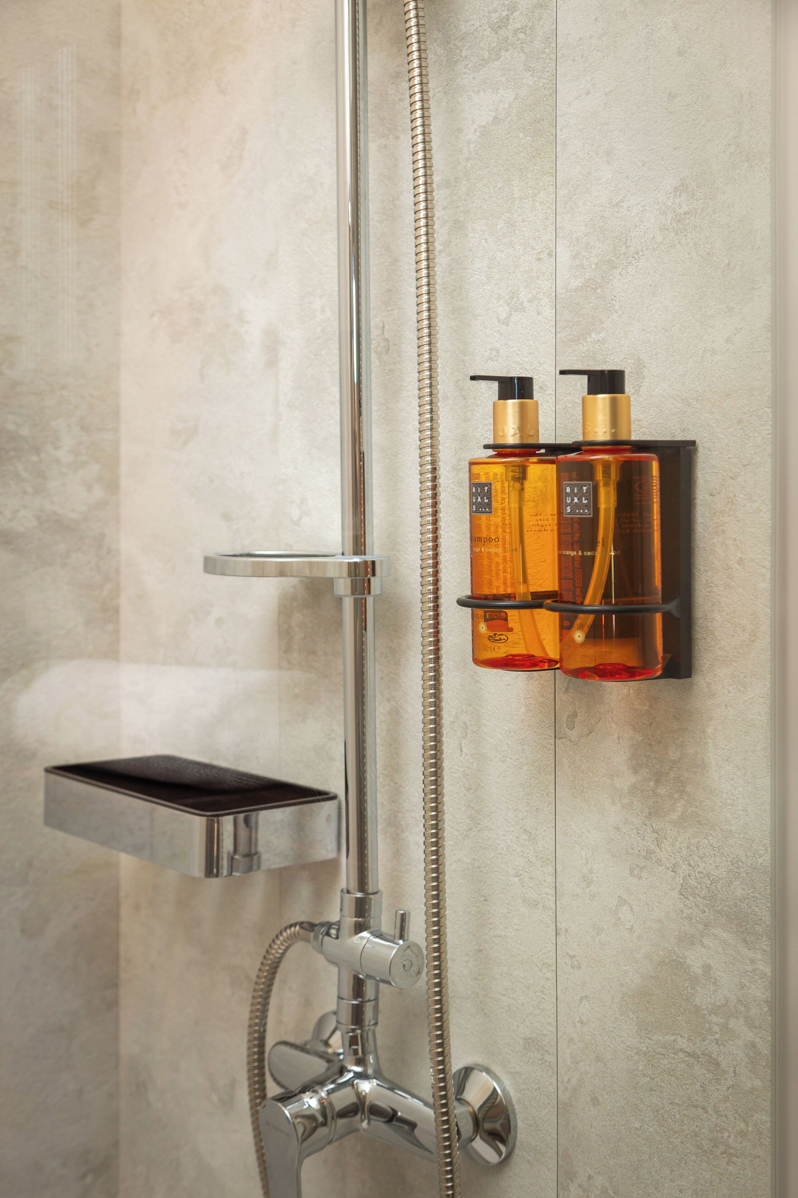 A shower with a chrome faucet, a handheld showerhead, and two bottles of shampoo and conditioner mounted on the wall.