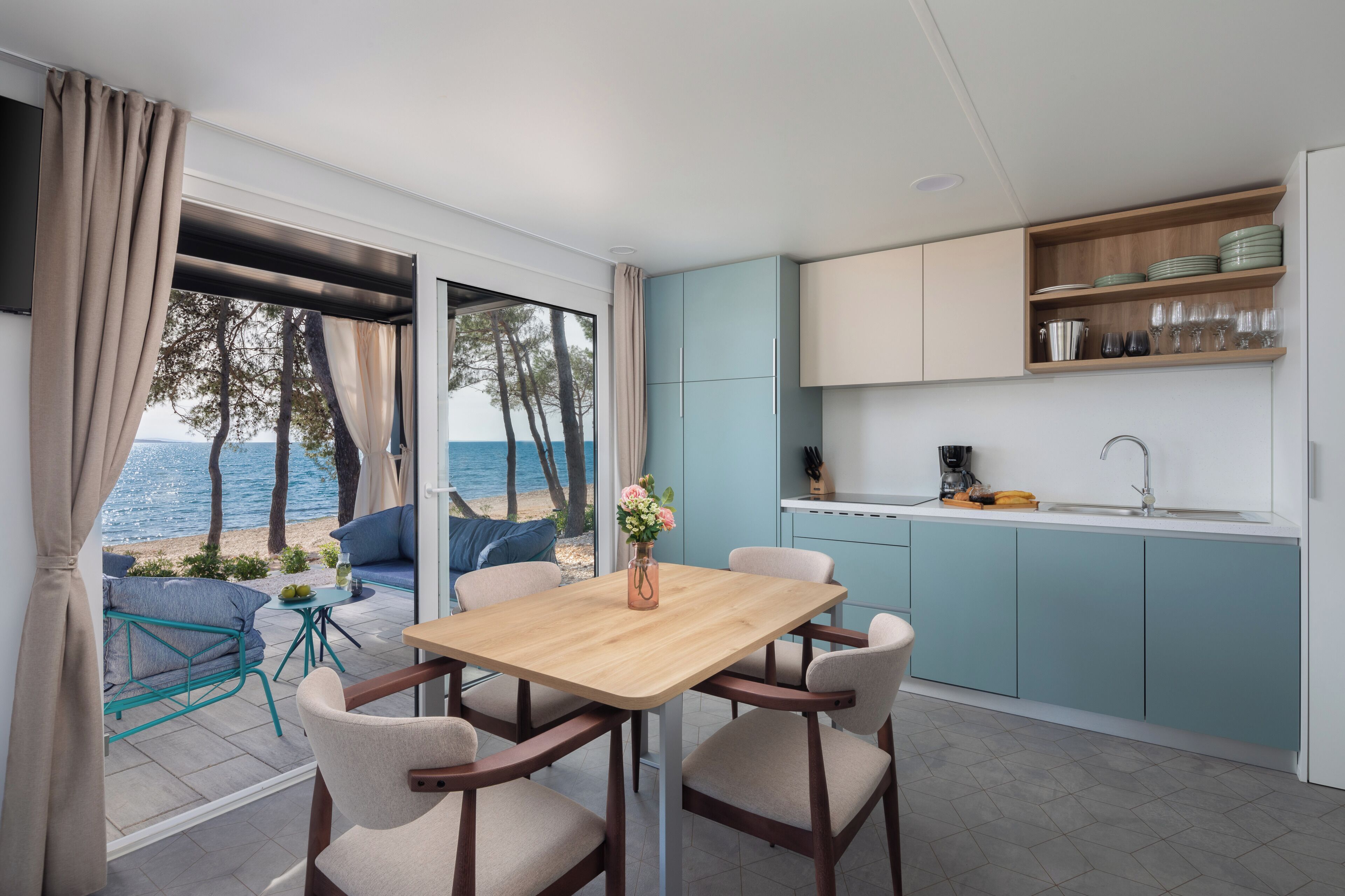 A modern kitchen with a view of the sea, a dining area with a table and chairs, and a small island with a coffee machine.