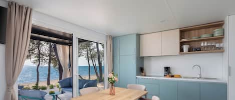 A modern kitchen with a view of the sea, a dining area with a table and chairs, and a small island with a coffee machine.