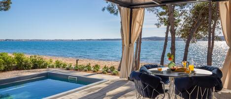 A poolside area with a view of the sea, a table with chairs, and a small pool.