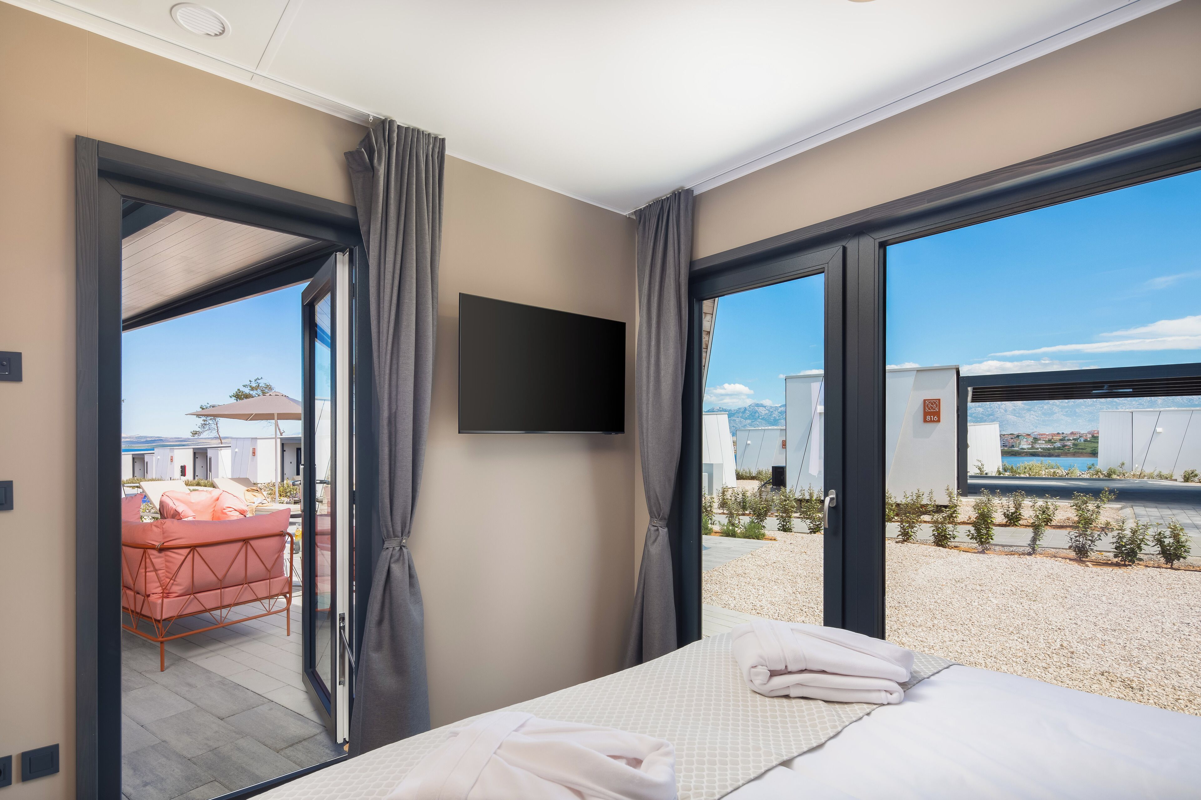 A modern hotel room with a large bed, a flat-screen TV, and a view of a pool and outdoor area.