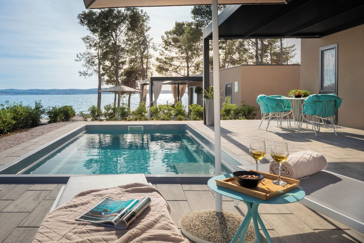 A poolside area with a view of the sea, a table with drinks, and a magazine.