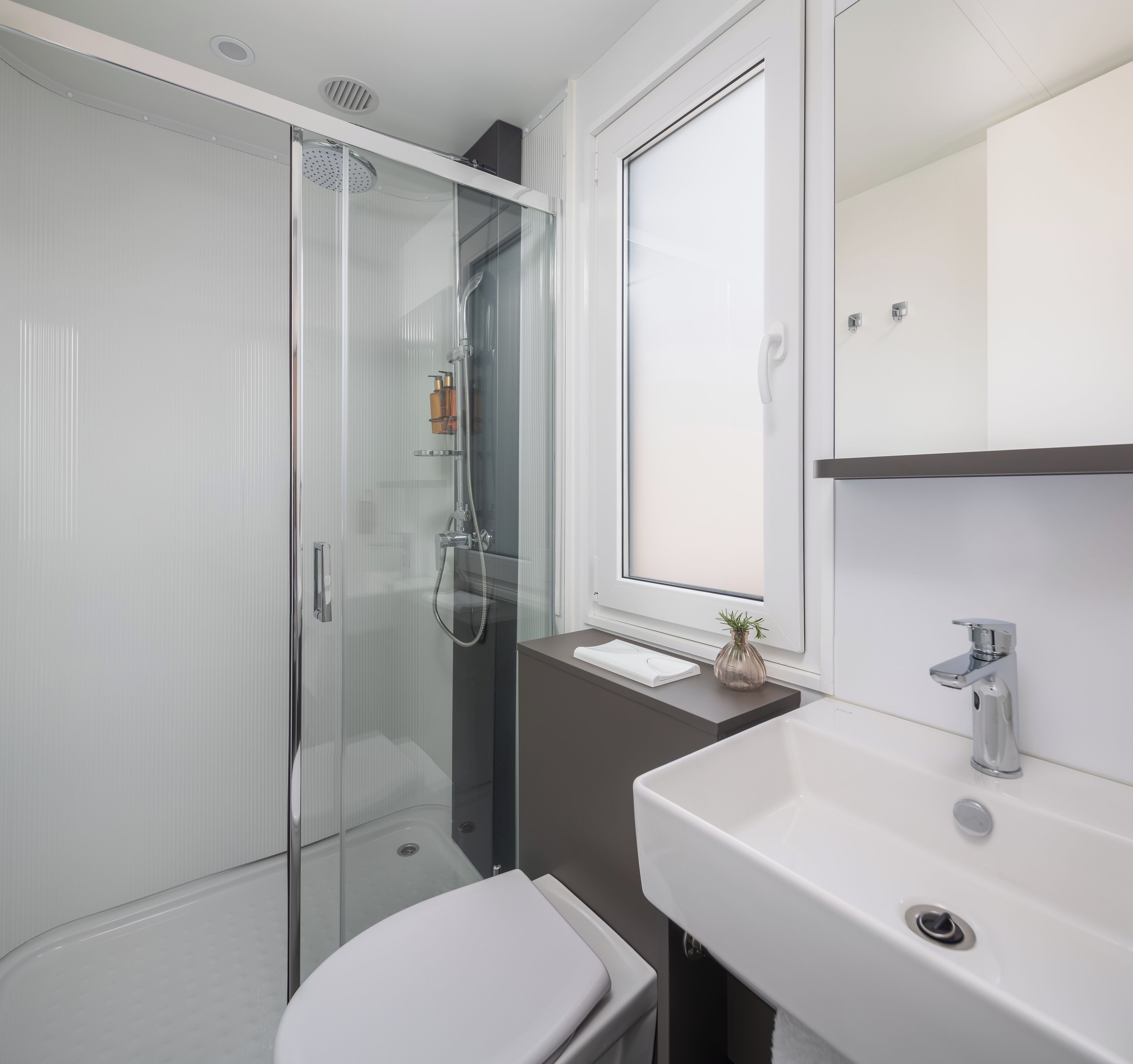 Een moderne badkamer met een glazen douchecabine, een wit toilet en een wastafel met spiegel.