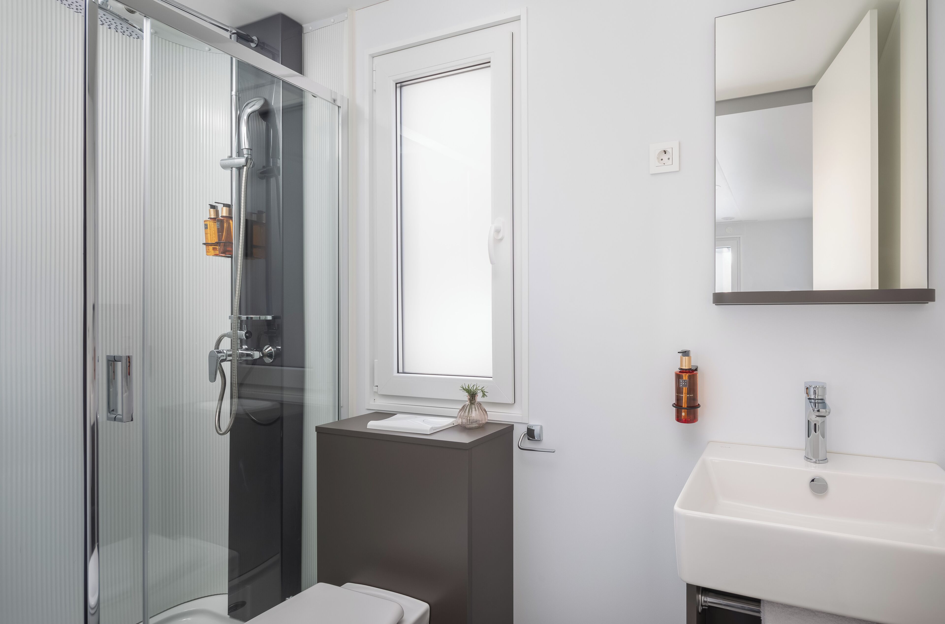 A modern bathroom with a glass shower enclosure, a sink, and a mirror.
