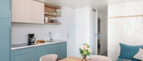 Cozinha compacta com armários verde-água, uma cafeteira e um vaso com flores na mesa de jantar.