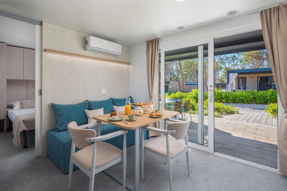 A modern room with a sofa, a dining table with chairs, a breakfast setup, and a sliding glass door leading to an outdoor area.