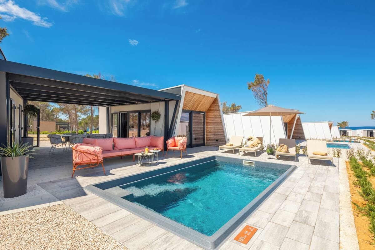 Ein moderner Außenpoolbereich mit einem rechteckigen Pool, Liegestühlen, einer rosa Couch und einer überdachten Sitzecke.