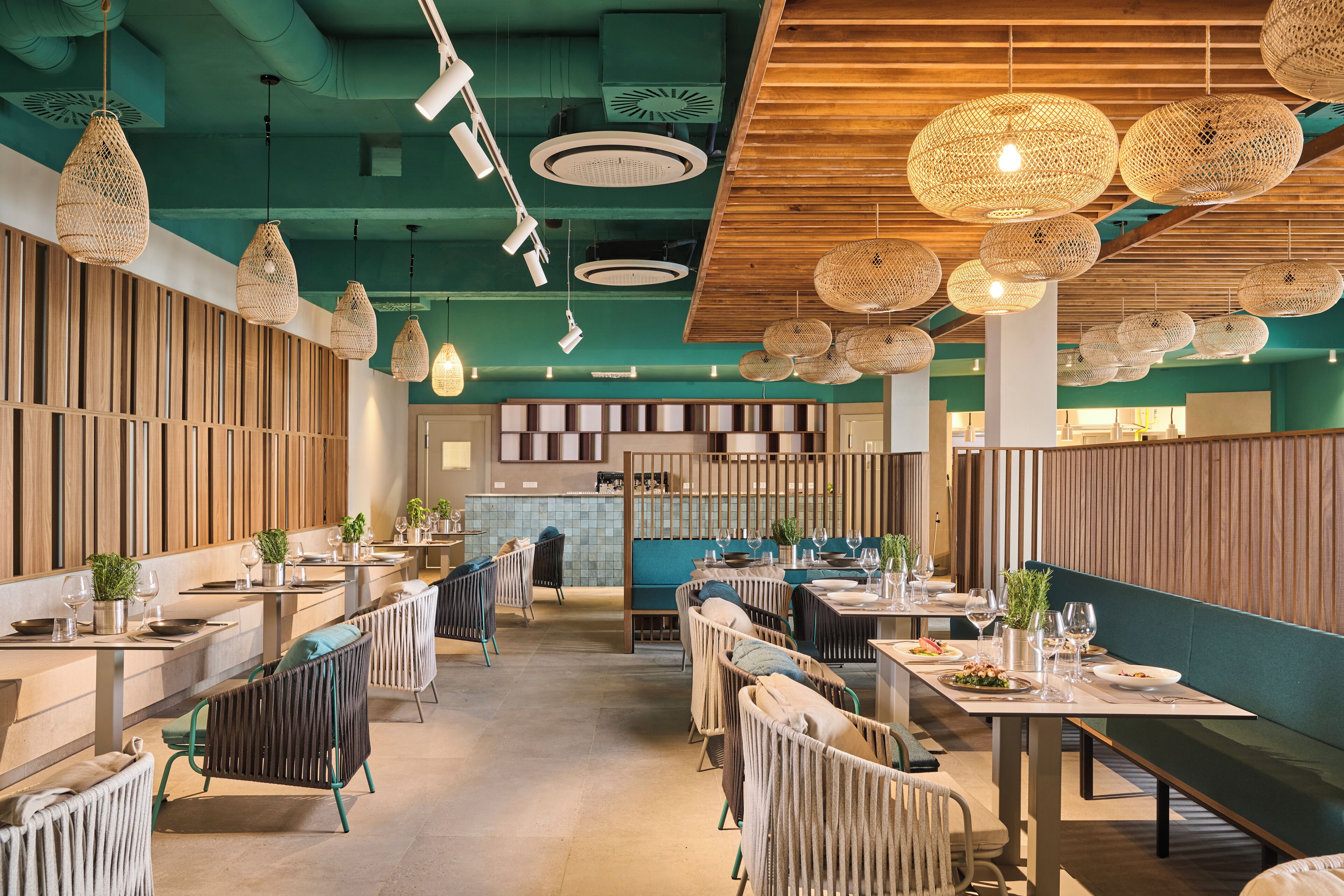En modern restauranginteriör med högt i tak, flätade lampor och en blandning av olika sittarrangemang, inklusive bord och avskilda sittplatser.