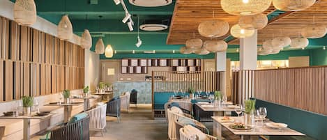 Ein modernes Restaurantambiente mit hohen Decken, gewobenen Leuchten und verschiedenen Sitzmöglichkeiten, darunter Tische und Sitzbänke.