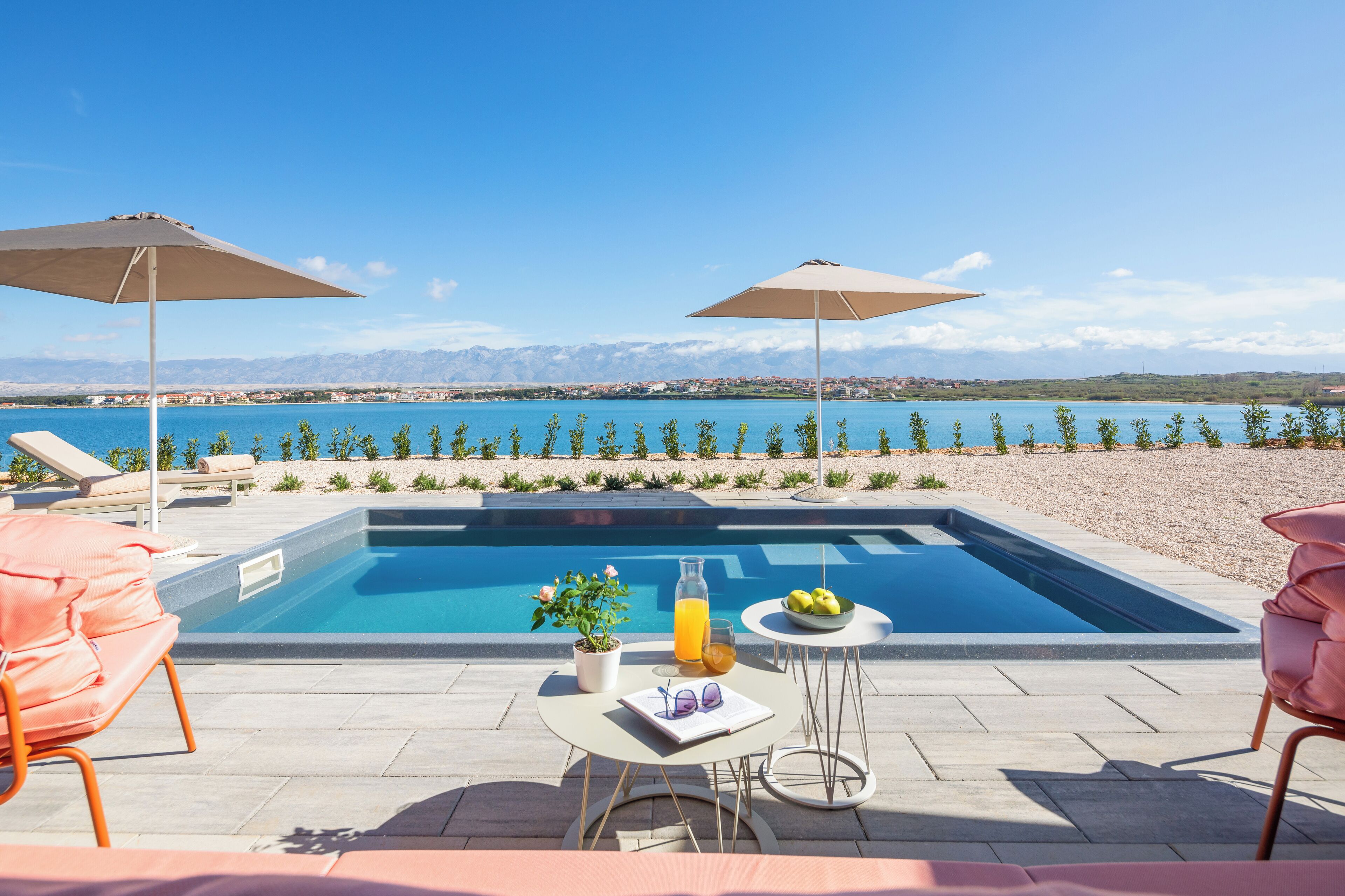 A pool area with lounge chairs, umbrellas, and a table with a drink and flowers.