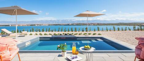 A pool area with lounge chairs, umbrellas, and a table with a drink and flowers.