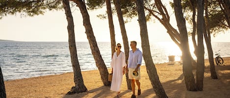 A couple walking on a sandy beach with trees and the sea in the background.