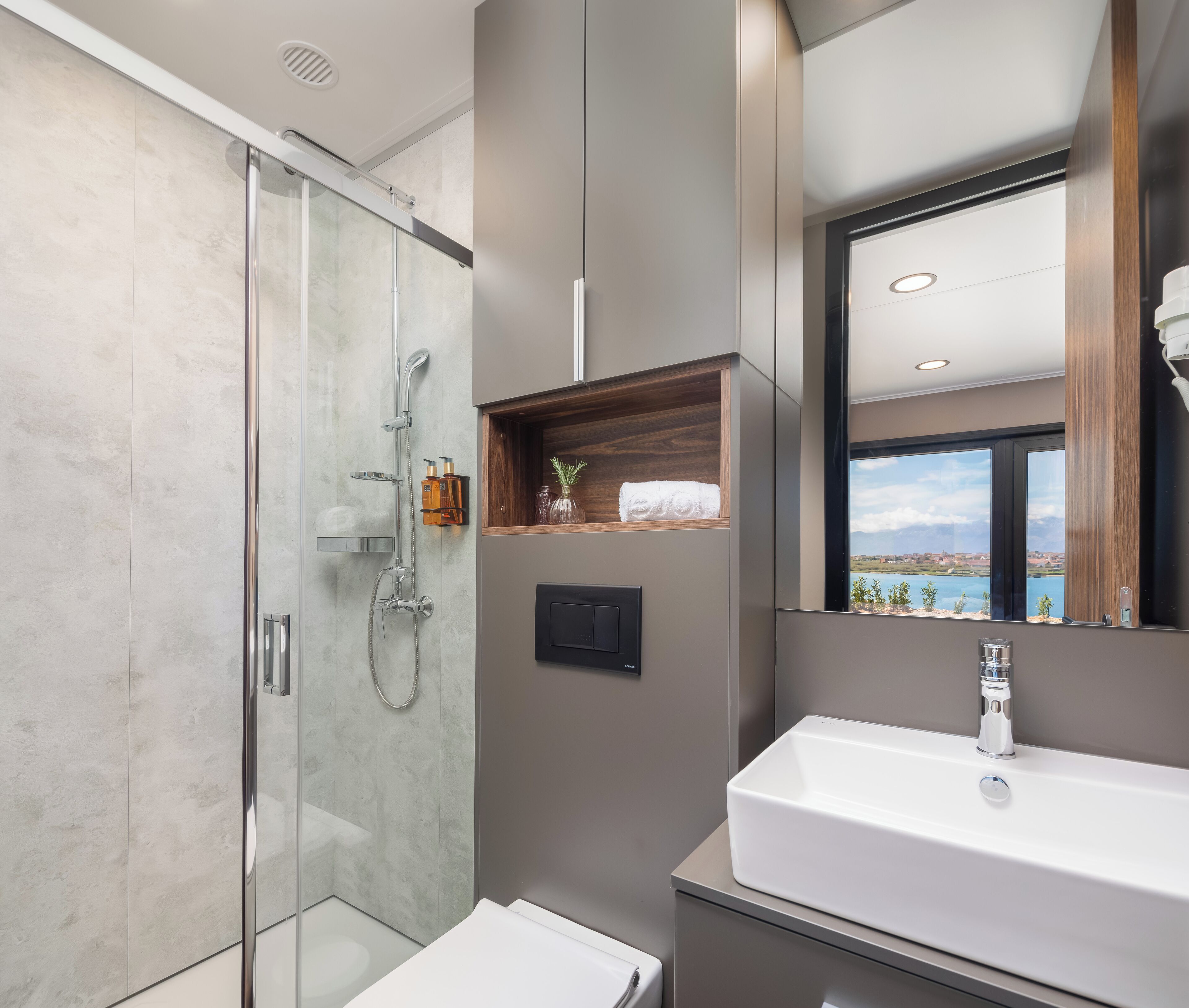 A modern bathroom with a glass shower enclosure, a large sink, and a mirror reflecting a scenic view.