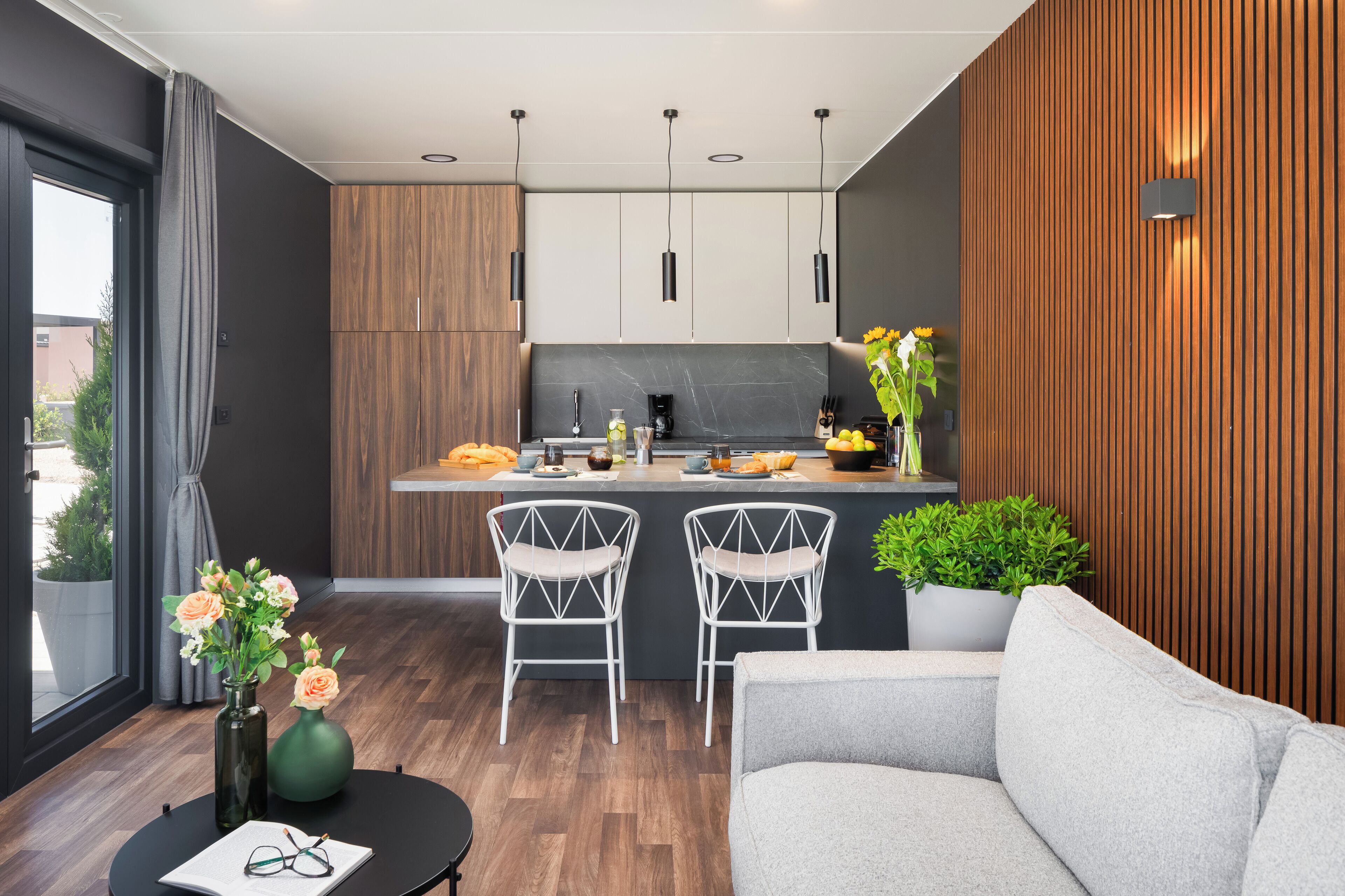 Een moderne keuken met houten kastjes, een marmeren aanrechtblad en twee barkrukken.