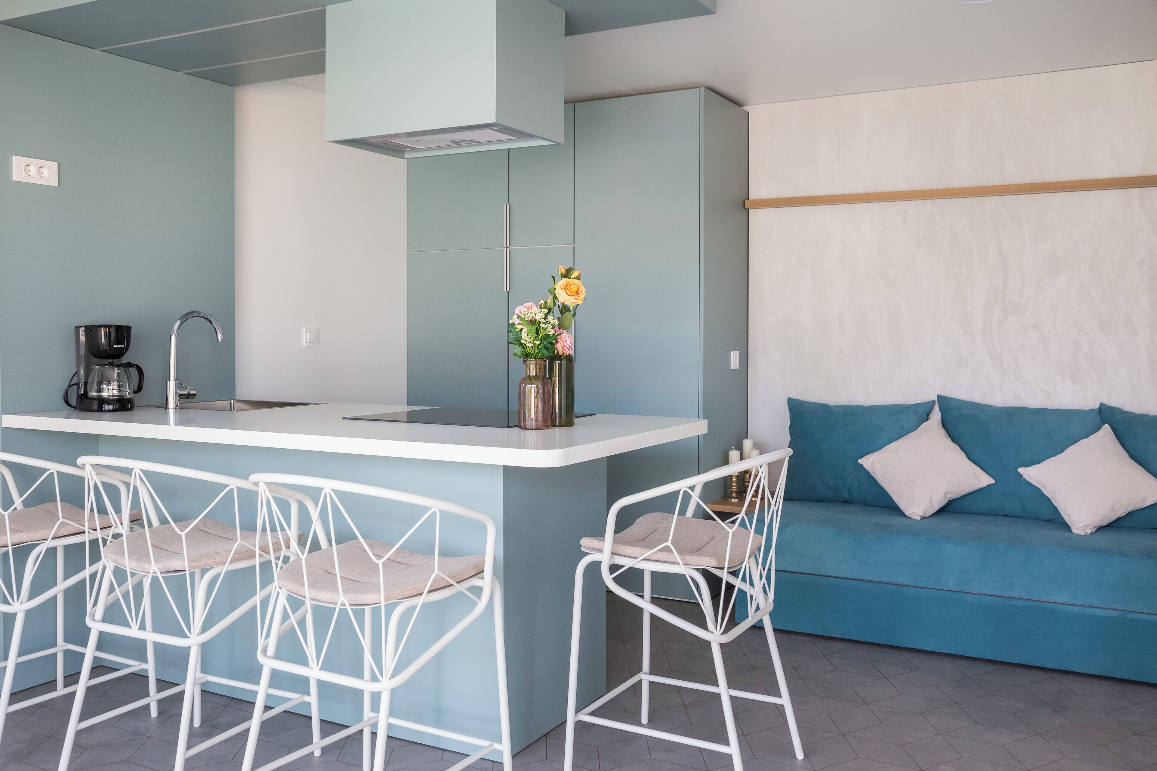 Eine moderne Küche mit Barbereich, weißen Barhocker, einem blauen Sofa und einer Vase mit Blumen.