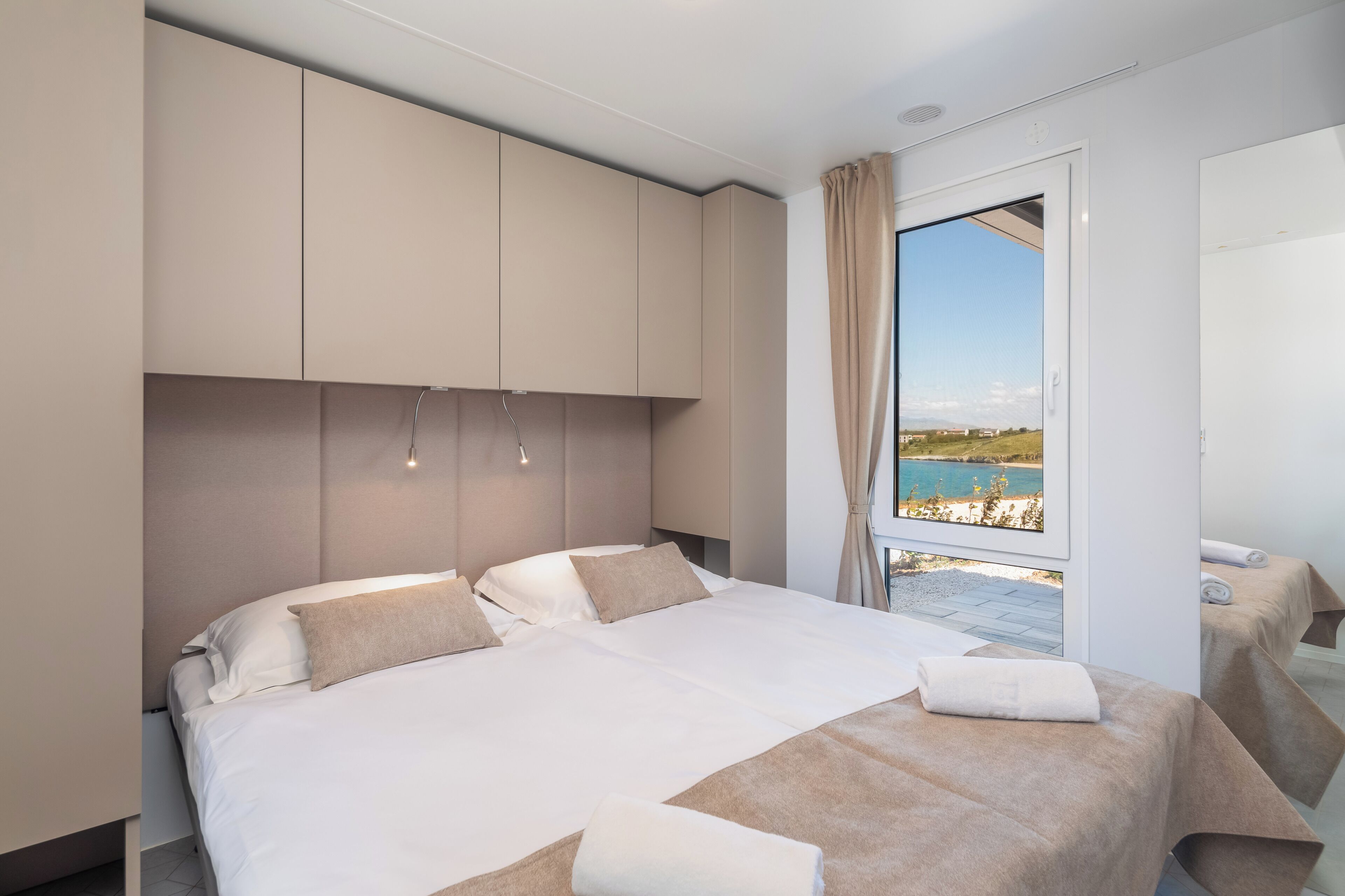 Een moderne slaapkamer met een groot bed, een inbouwkast en uitzicht op een kustlandschap.