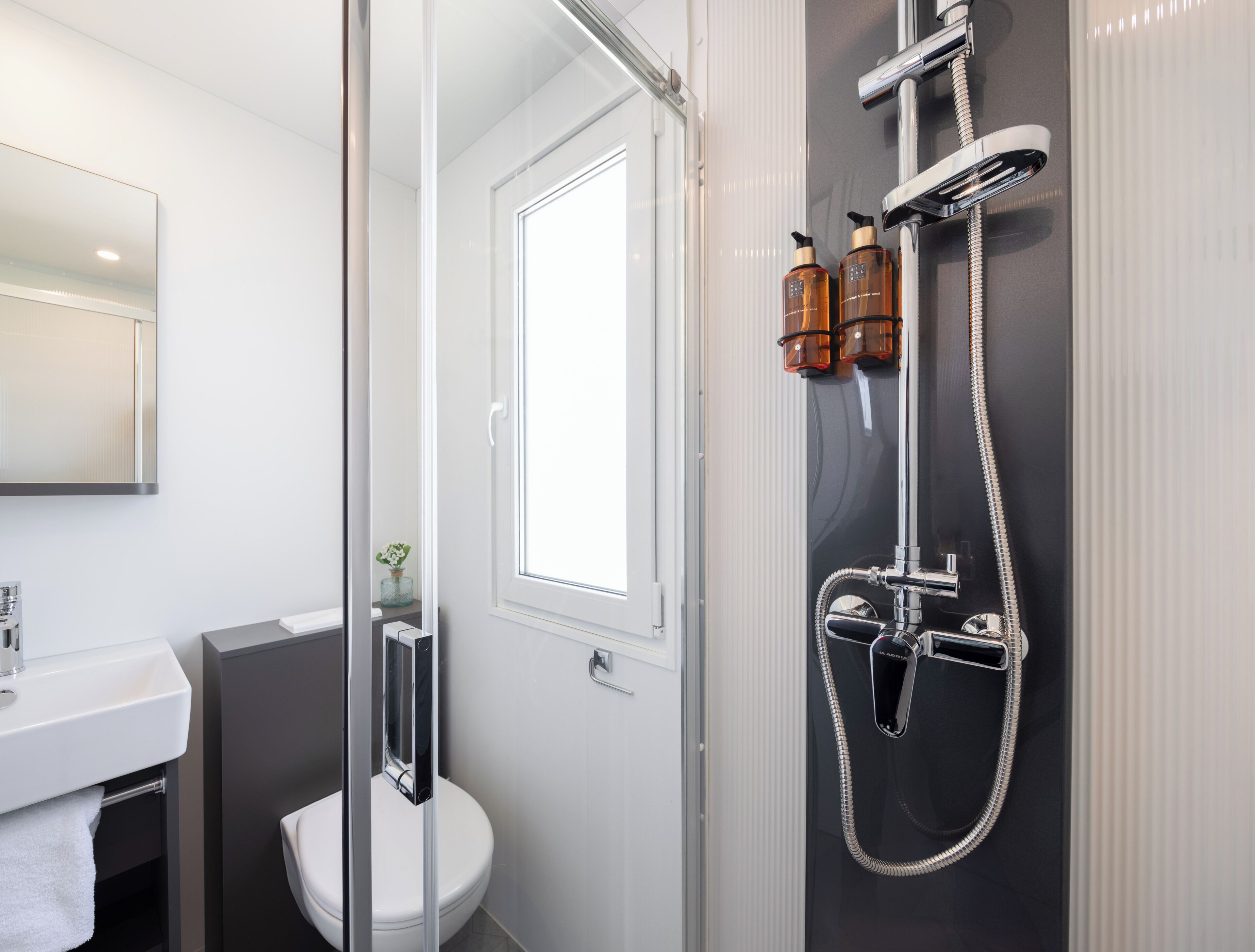 Ein modernes Badezimmer mit einer gläsernen Duschkabine, einer weißen Toilette und einem Waschbecken mit Handtuch.