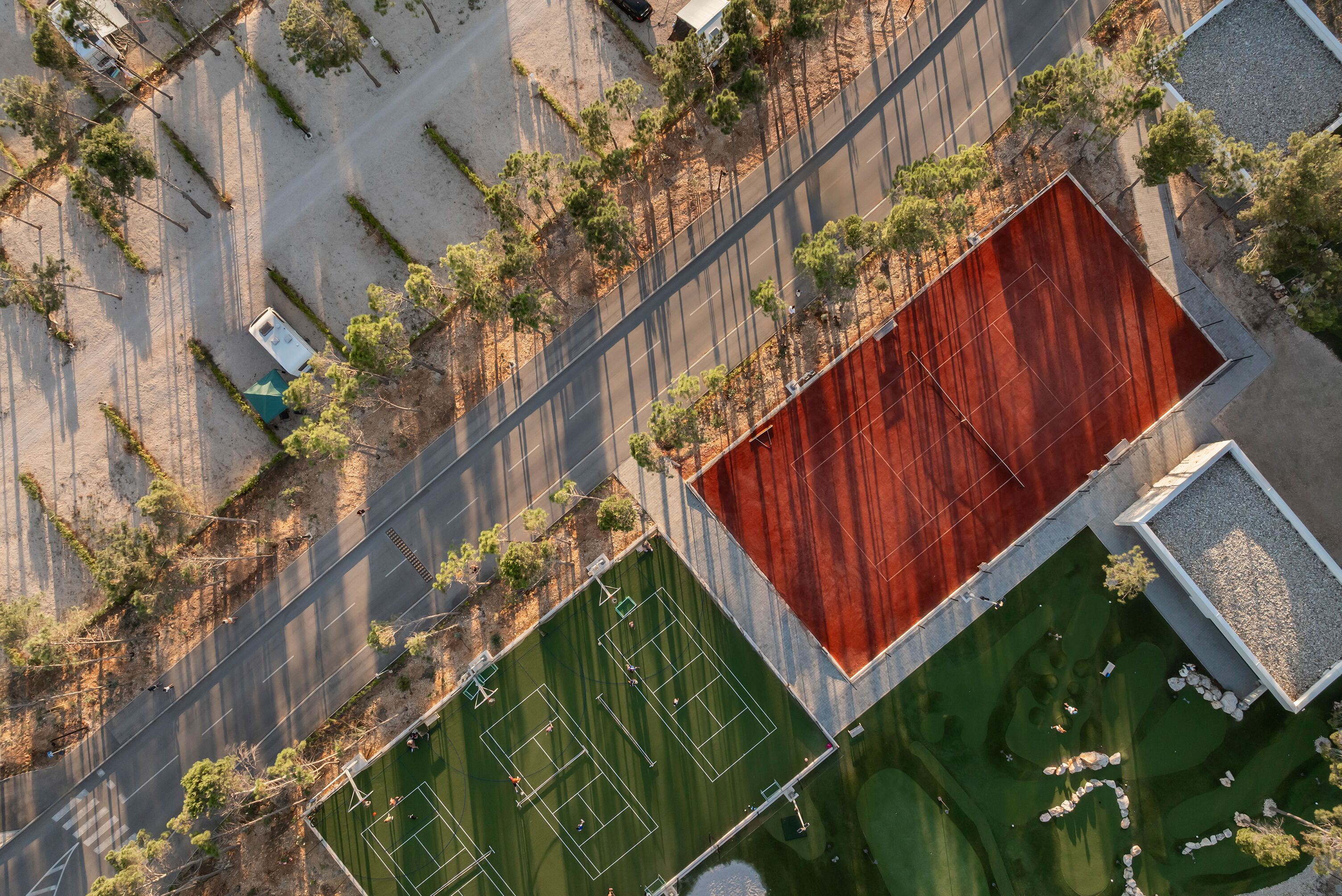 An aerial view of a sports complex with tennis courts, a parking area, and surrounding greenery.