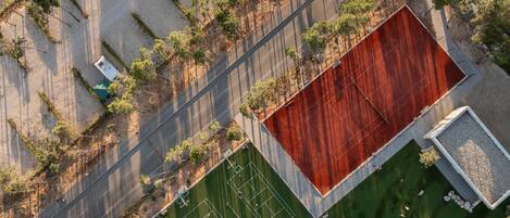 An aerial view of a sports complex with tennis courts, a parking area, and surrounding greenery.