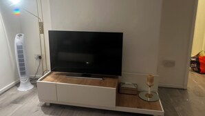 Una sala moderna con una televisión de pantalla plana sobre un mueble de madera, un aire acondicionado blanco y una pequeña mesa con una vela.