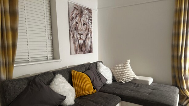 Una sala de estar moderna con un sofá seccional, un cuadro decorativo de un león y una ventana con persianas.