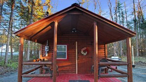 A wooden cabin with a red deck, a door with a wreath, and a window. - Travelers Haven (Whitefield)