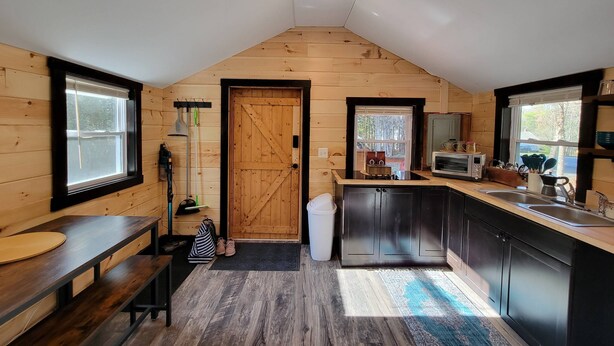A kitchen with wooden walls, a large window, a sink, and a microwave. - Travelers Haven (Whitefield)