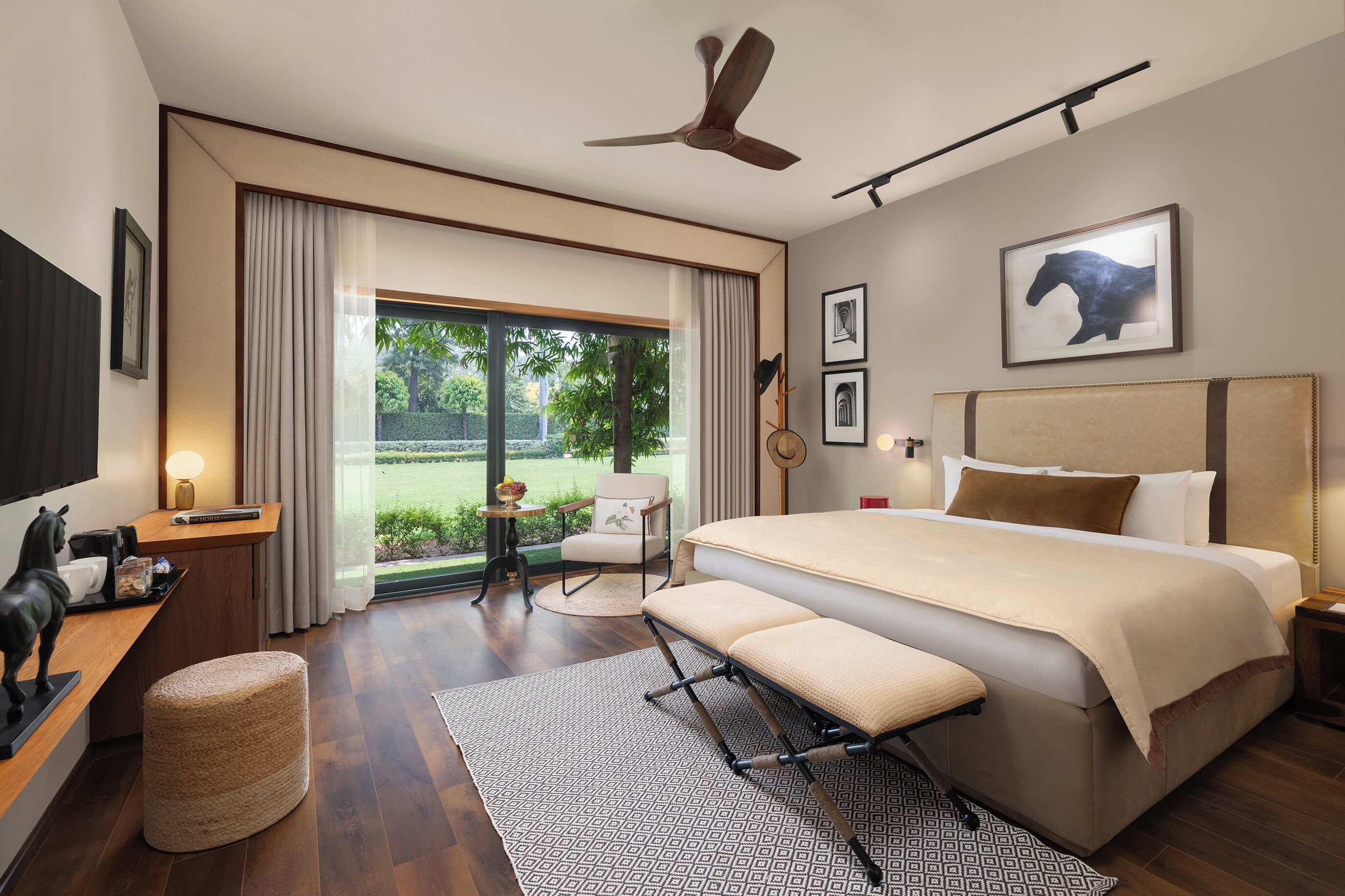 Habitación de hotel moderna con una cama grande, ventilador de techo, escritorio con lámpara, una silla y vistas al exterior.