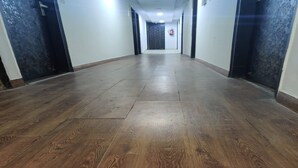 A long, narrow hallway with wooden flooring and black doors on both sides. - Hotel The Green Arrow (New Delhi)