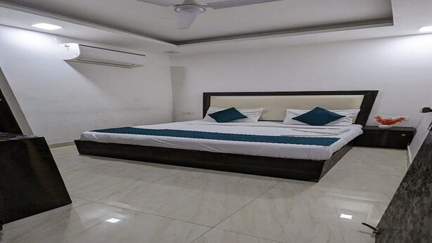 A modern bedroom with a large bed, a ceiling fan, and a nightstand with a vase. - Hotel The Green Arrow (New Delhi)