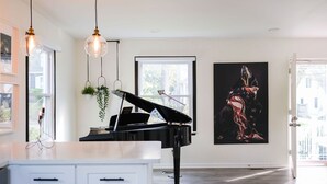 Un salon moderne avec un grand piano, des luminaires suspendus, une grande peinture abstraite et une vue sur l’extérieur.